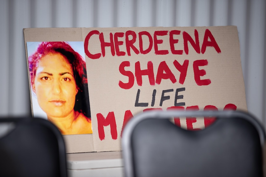 A cardboard sign with a woman's face and red writing on it.