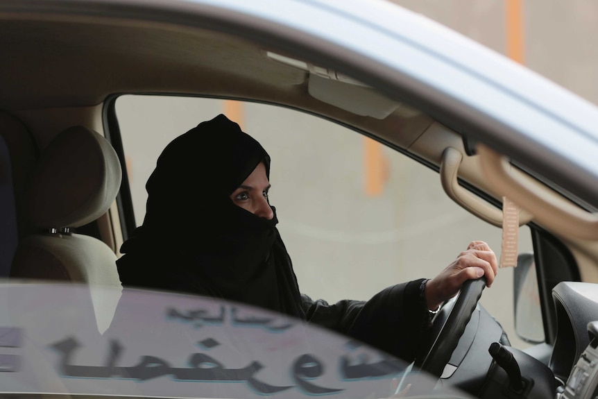 A Saudi woman wearing a head covering driving a car.