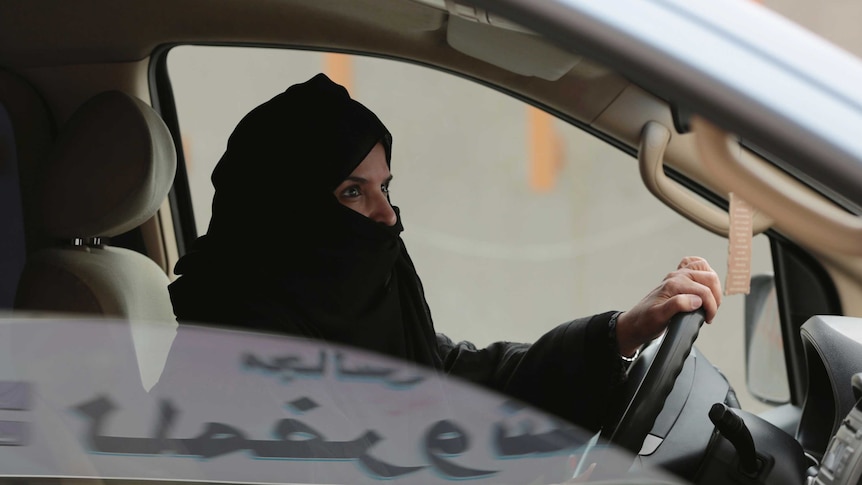 A Saudi woman wearing a head covering driving a car.