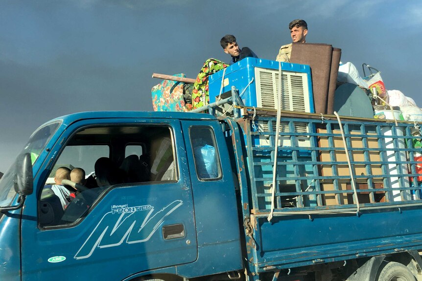 Two young men sit on top of a truck packed with furniture.