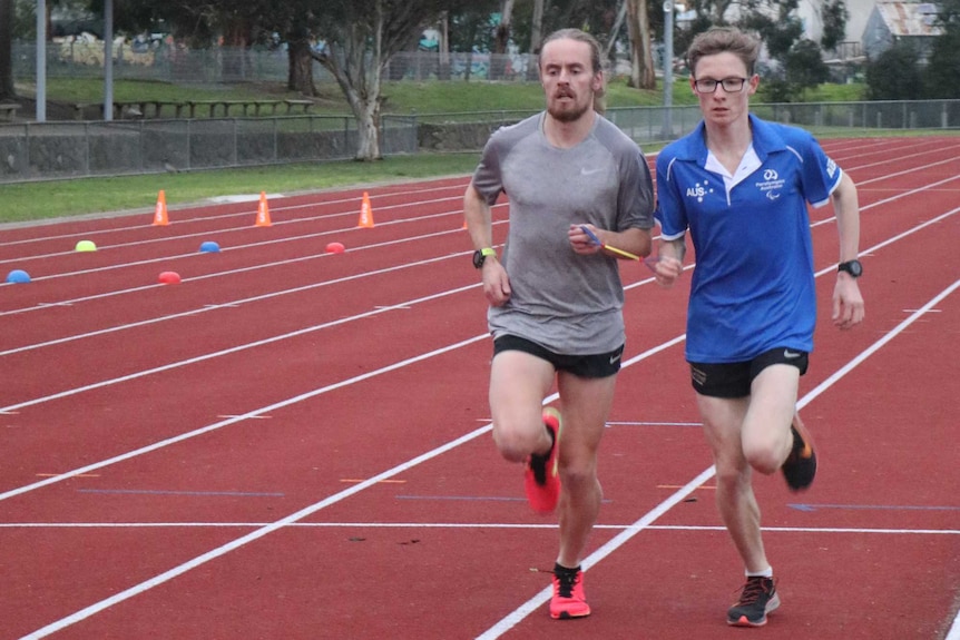 Jaryd Clifford and his running guide Tim Logan each hold onto one end of a short guide rope as they run on a track.