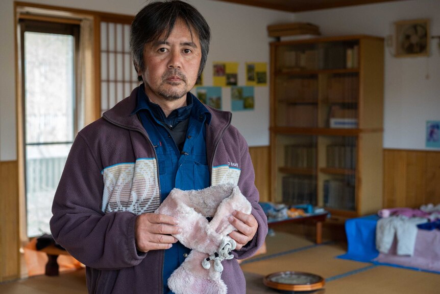 A Japanese man holds a fluffy pink scarf with a Mikey Mouse doll attached