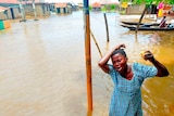 Woman in blue dress appears distressed with arms in air surrounded by flood waters. 