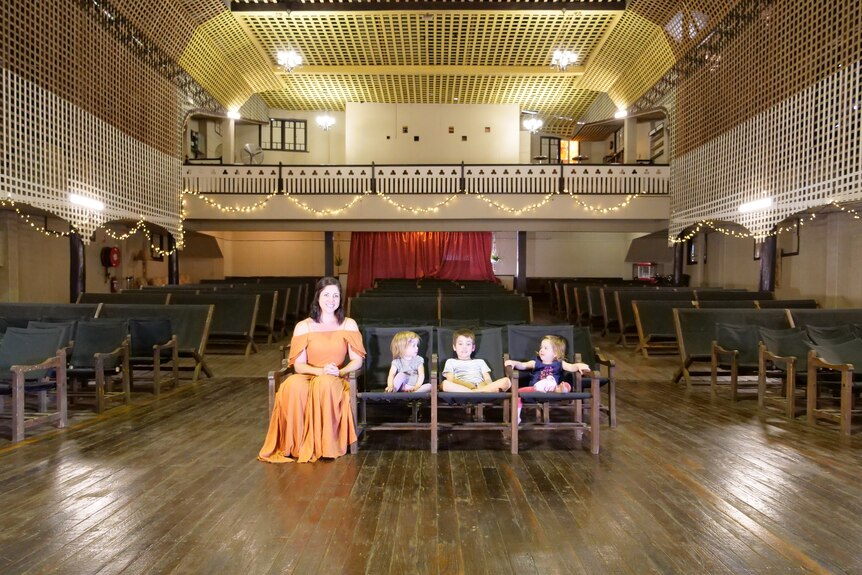 A woman and her three children sit in the wooden front row seats of an old theatre