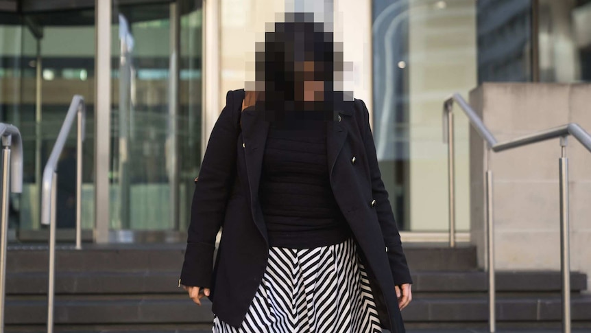 A woman in a black coat and black and white striped skirt walks down the steps in front of court.