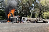 A car burns on a road in a bushy area.