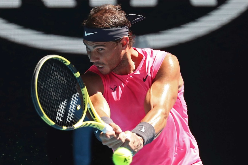 A pink-shirted tennis player grimaces as he hits a return during the Australian Open.