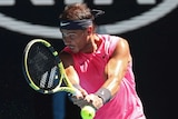 A pink-shirted tennis player grimaces as he hits a return during the Australian Open.