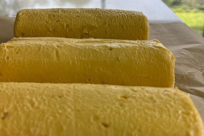 Deep gold coloured rolls of butter on a stainless steel bench.