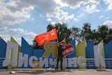 A man raises a Soviet-era flag at a yellow and blue monument that says I love Lysychansk