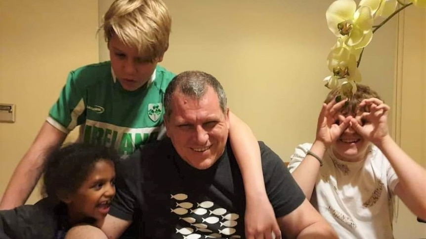 Robert Pether surrounded by his three children at a table as they celebrate a birthday with a cake.