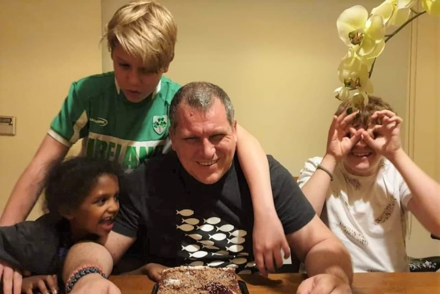 Robert Pether surrounded by his three children at a table as they celebrate a birthday with a cake.