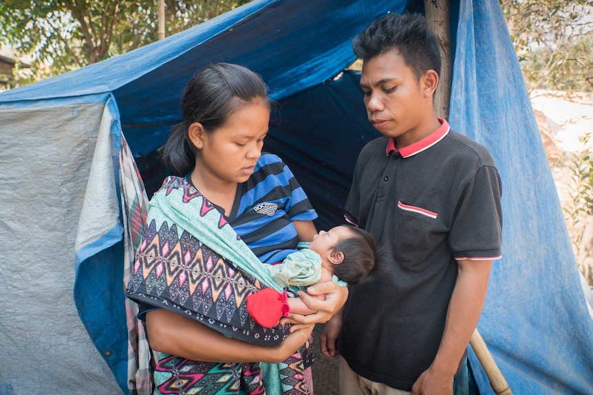 A mother holds her baby in front of a tent