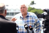 a man in a check blue and yellow shirt speaking to media