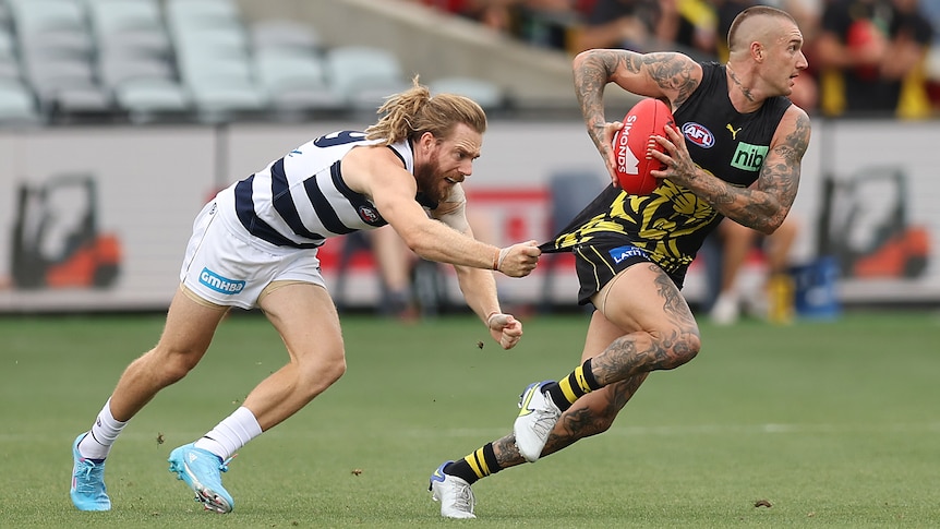 A Richmond AFL player holds the ball as he tries to get away from a Geelong opponent.