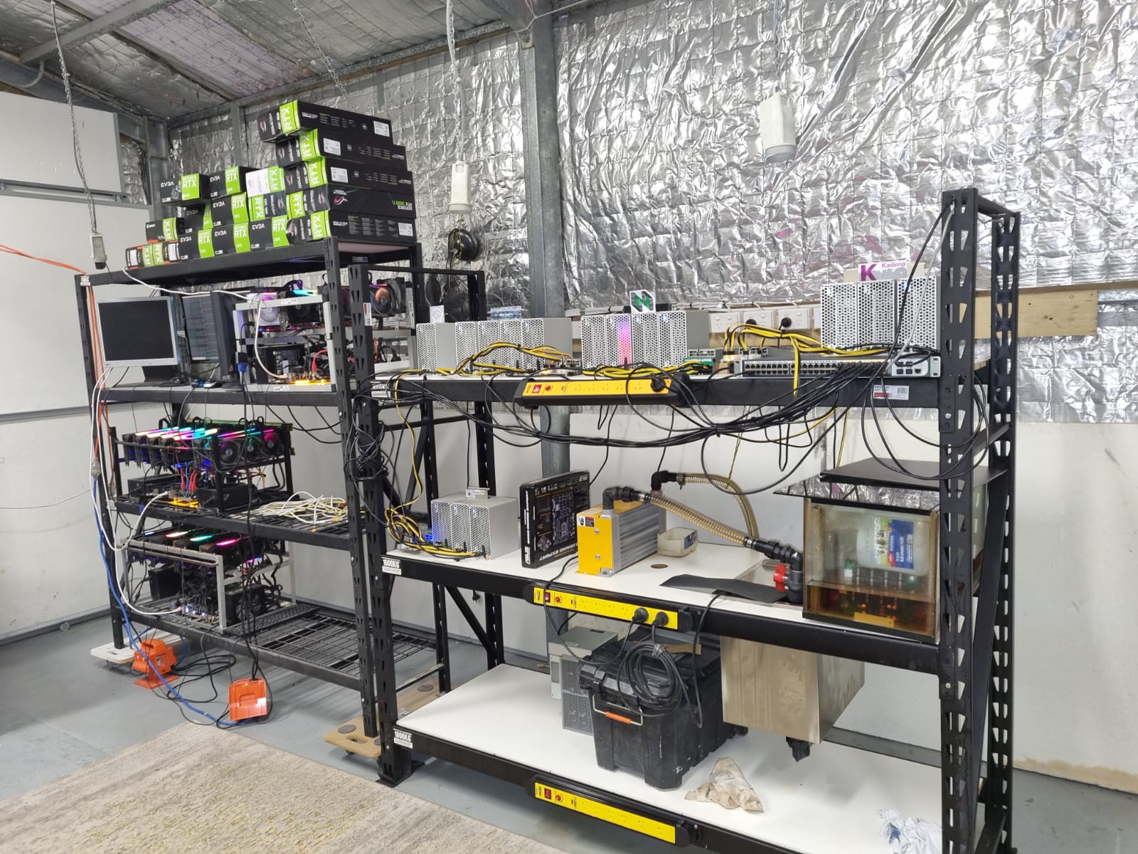 Two shelves in an insulated shed with electrical equipment, computers and cords.
