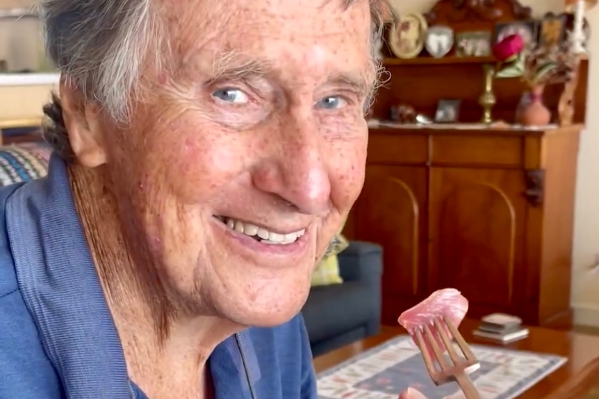 A man holds up a fork while looking at the camera.