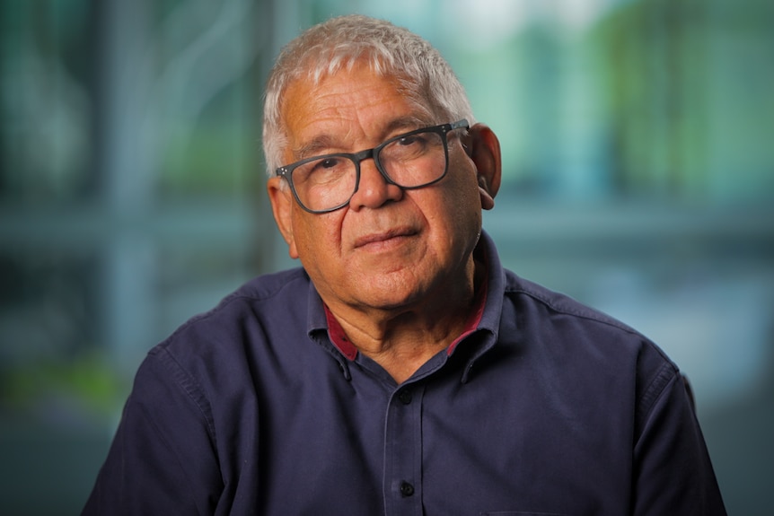An Indigenous man wearing a navy shirt and glasses looking into the camera. 
