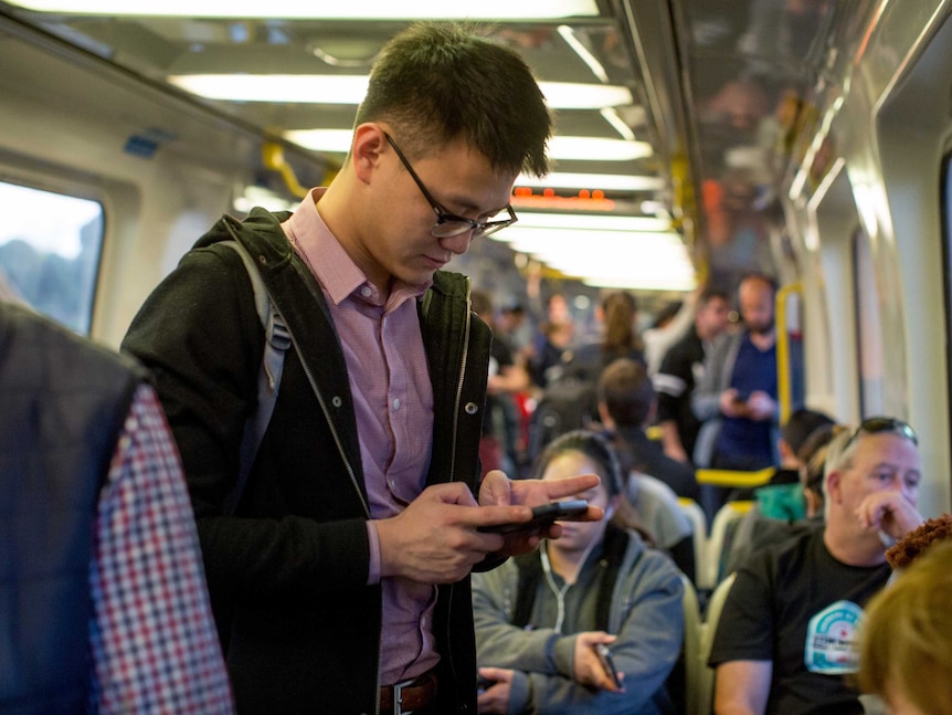 Johhny looks at his mobile phone while standing on a busy Melbourne train