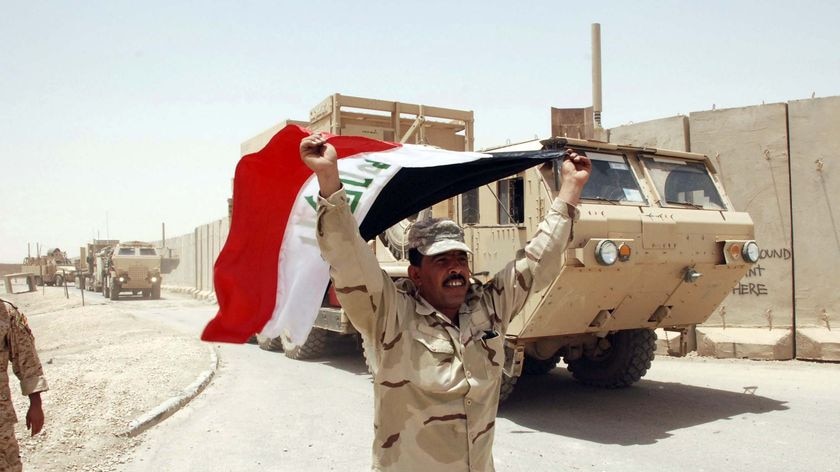 An Iraqi soldier waves an Iraqi flag in front of US military vehicles