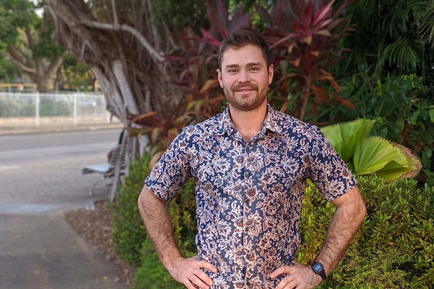 Young man in bold printed shirt standing in front of garden.