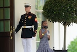 A military serviceman in formal dress holds open a door for a young black girl. 