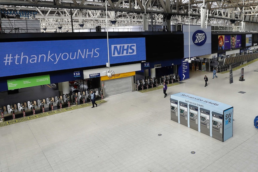 A large, near-empty train station with a giant "Thank you NHS" sign. The clock reads 9:00