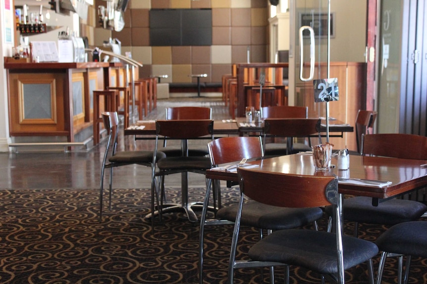 Two empty tables in a hotel dining room, in front of a row of empty bar stools.