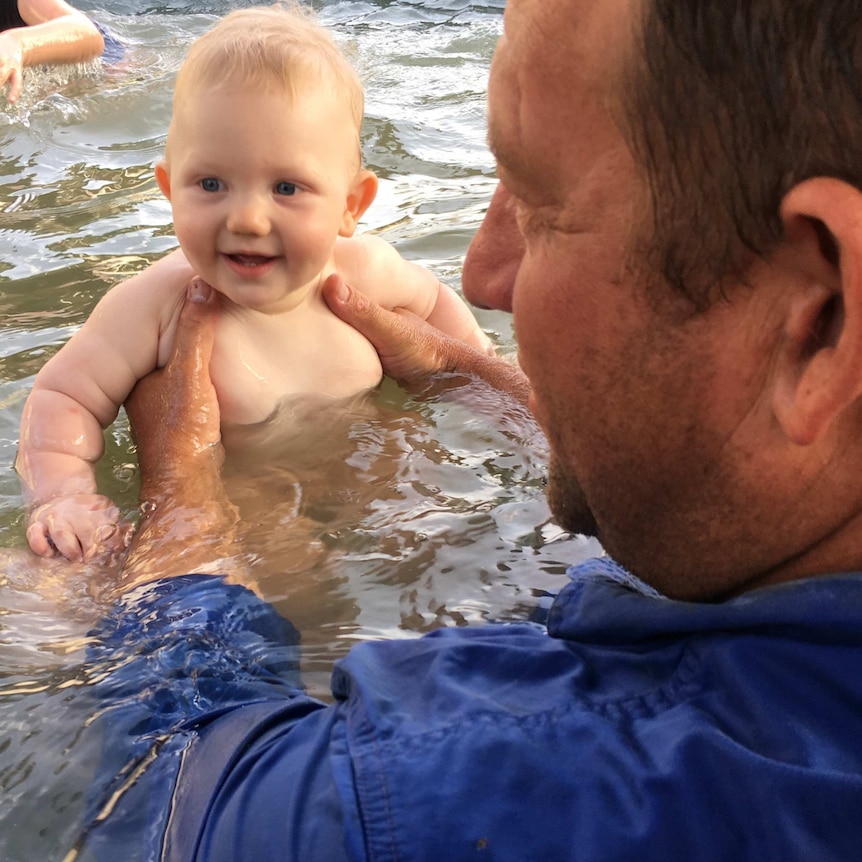 A baby enjoys a splash in the small pool with his dad.