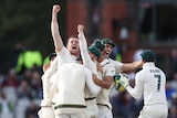 A group of cricketers hug as the man who took the winning wicket thrusts his fist to the sky.