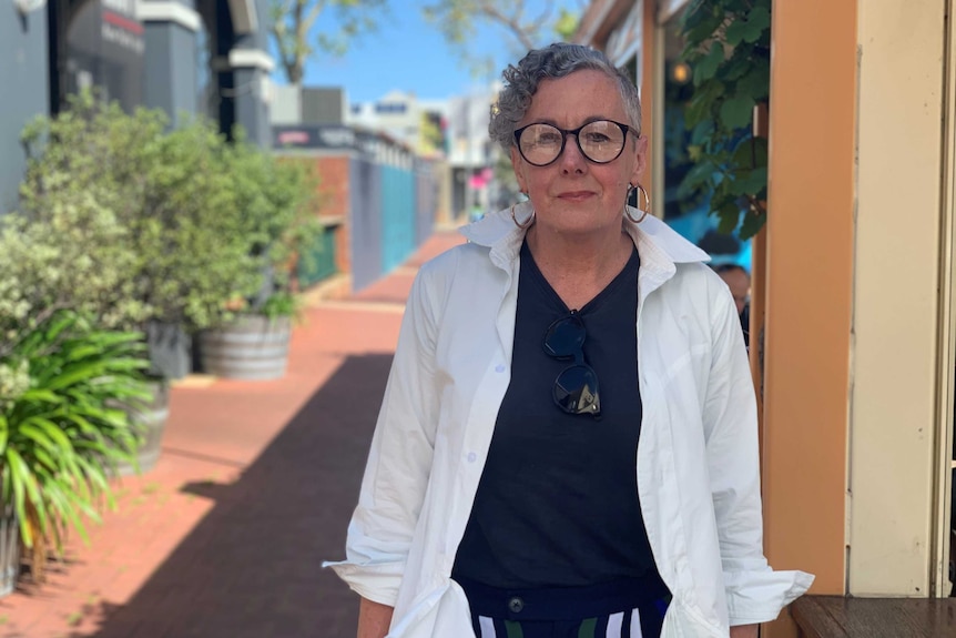 A women standing on a sidewalk with greenery around her and shops distant in the background