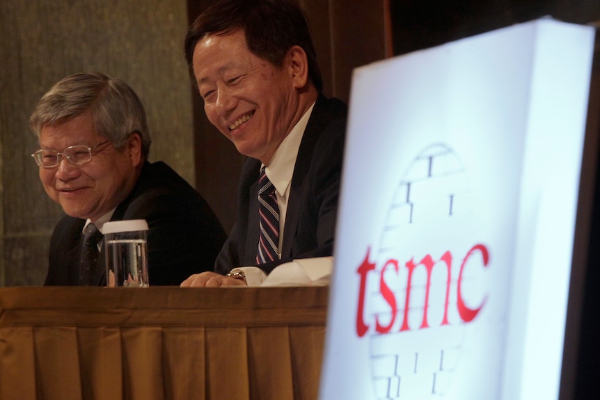 Two men sitting together with a light sign with TSMC logo on the table