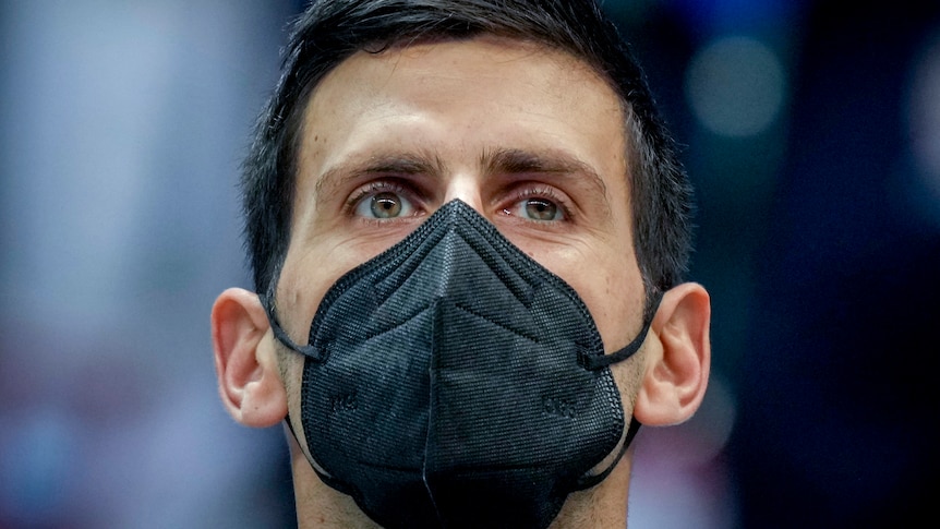 Tennis player Novak Djokovic wears a black face mask as he listens to national anthems.