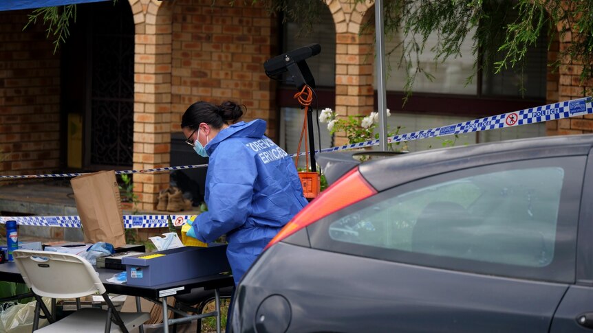 forensics worker at table with police tape and car and house