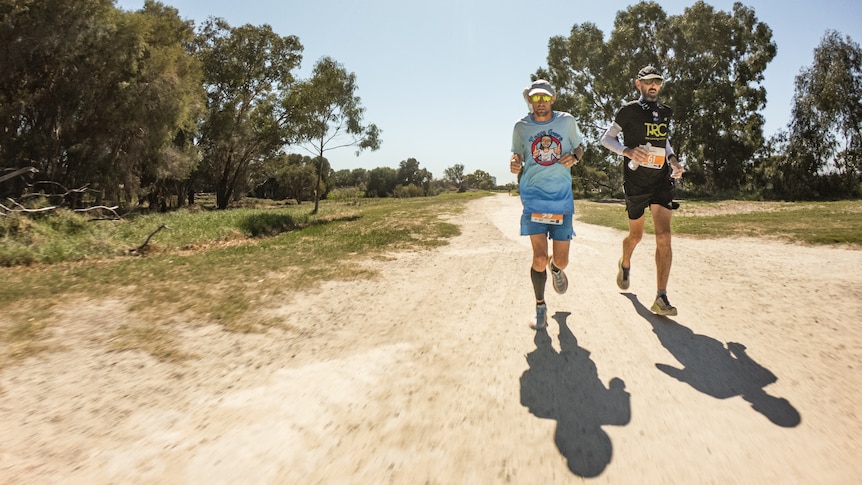 Two men running along dirt track surrounded by bushland