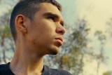 A young Indigenous man looks to the right of screen.