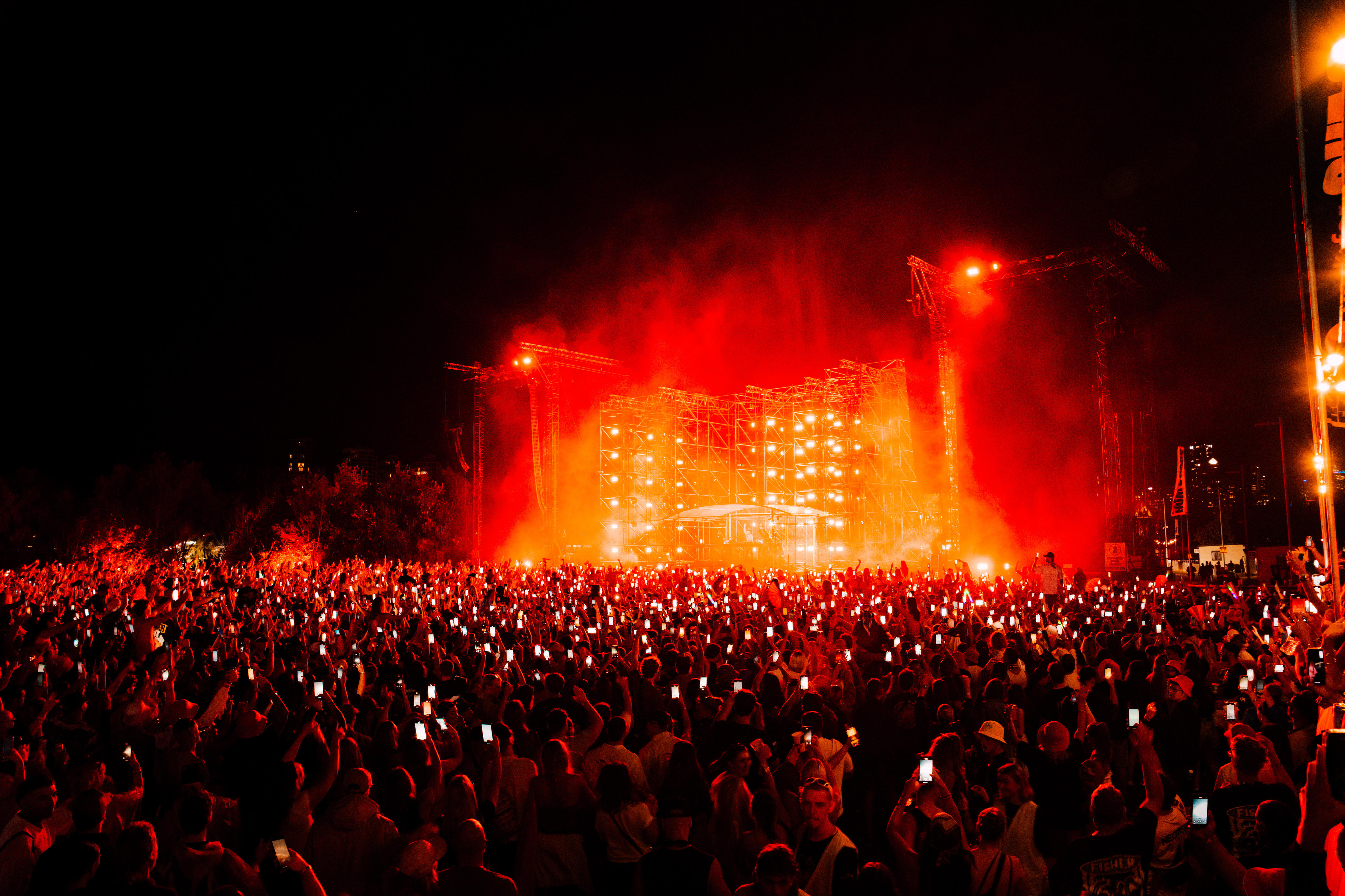 A large crowd of people holding phones up recording a stage at night with orange lighting