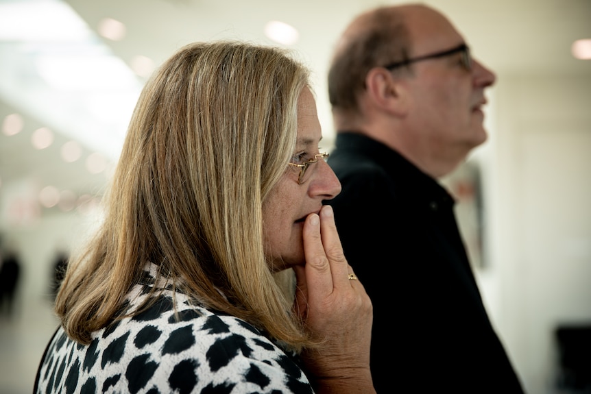 Two older people stand nervously in an airport