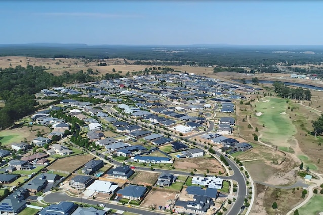 Aerial photo of a block of new-looking houses and a road with farmland around the development.