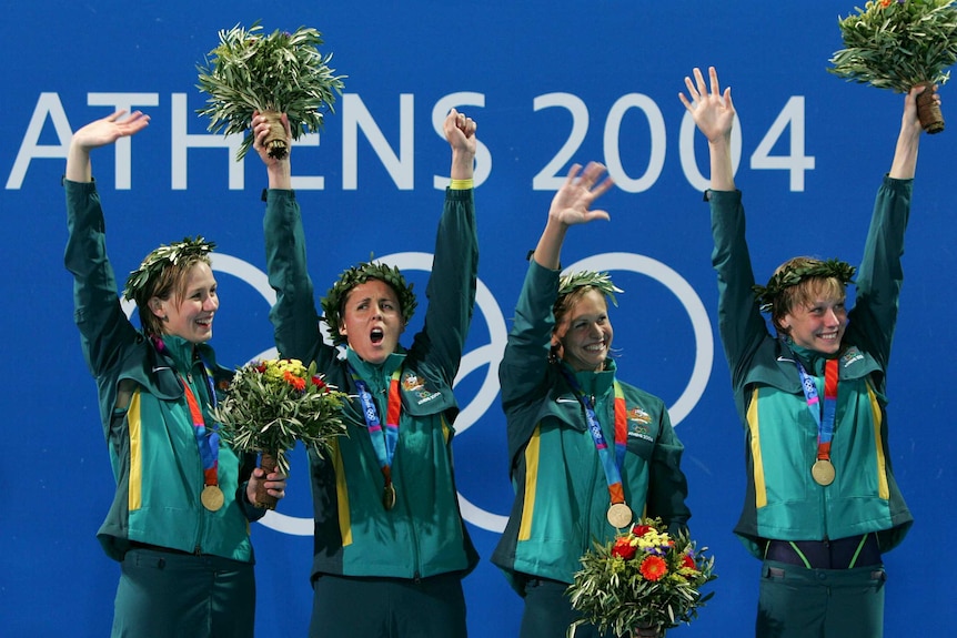A group of female swimmers wave flowers while holding relay gold medals at the Athens Olympics.