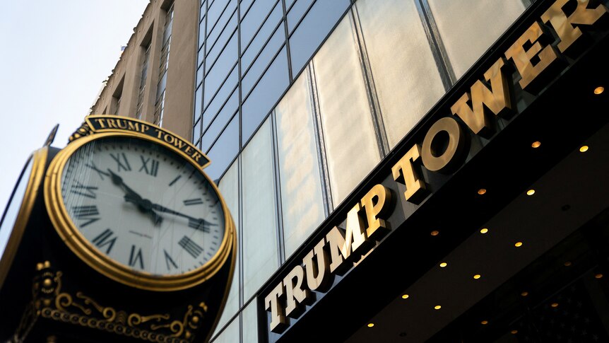 A tall, gold-tinged building towers over a vintage-style clock on a public street in New York.