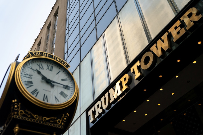 A tall, gold-tinged building towers over a vintage-style clock on a public street in New York.