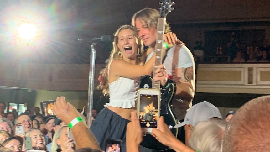 Country singer Keith Urban gives his guitar to a teenage girl on stage