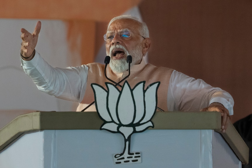 Indian Prime Minister Narendra Modi gestures as he speaks during an election campaign rally behihnd a lecturn.