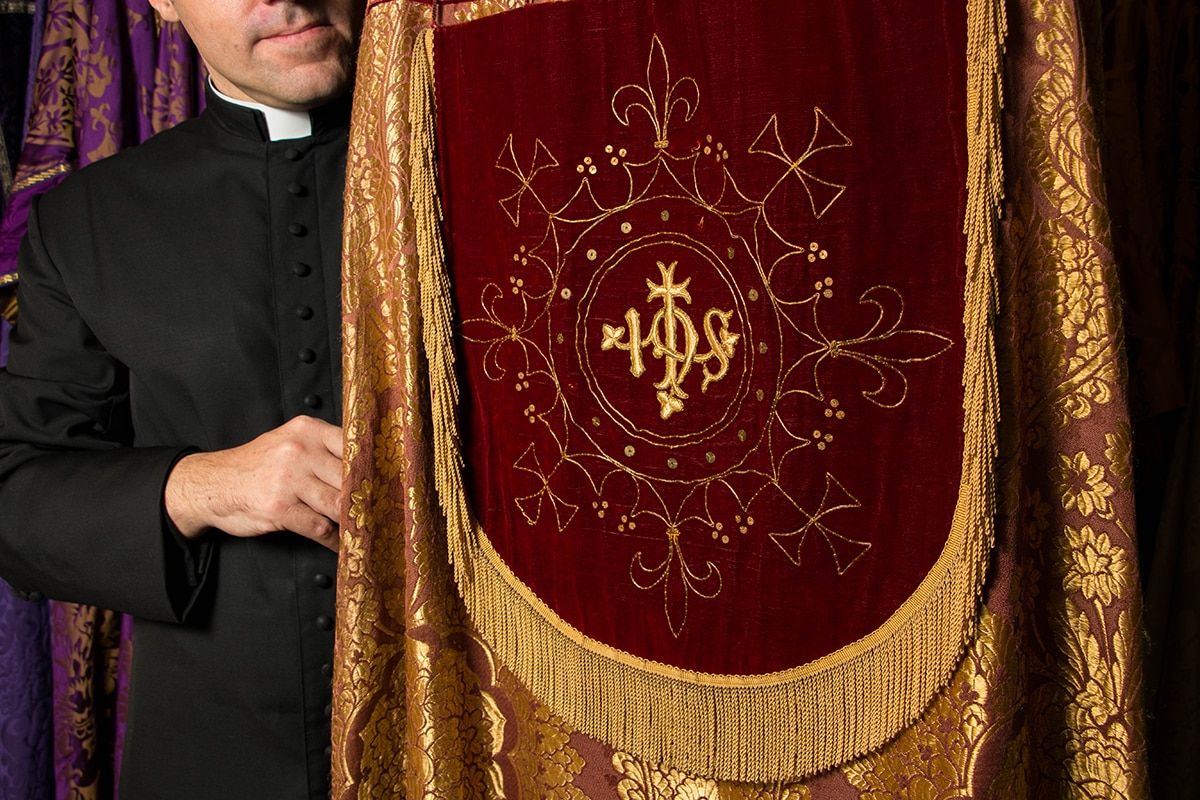 Rector Daniel Dries holding elaborate gold and red liturgical cloak known as a cope.