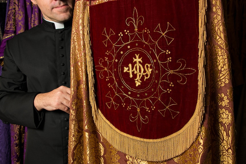 Rector Daniel Dries holding elaborate gold and red liturgical cloak known as a cope.