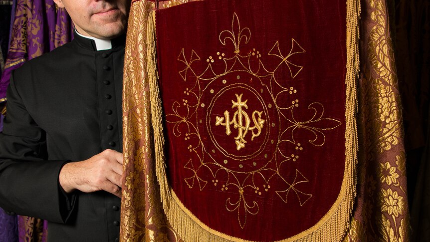 Rector Daniel Dries holding elaborate gold and red liturgical cloak known as a cope.