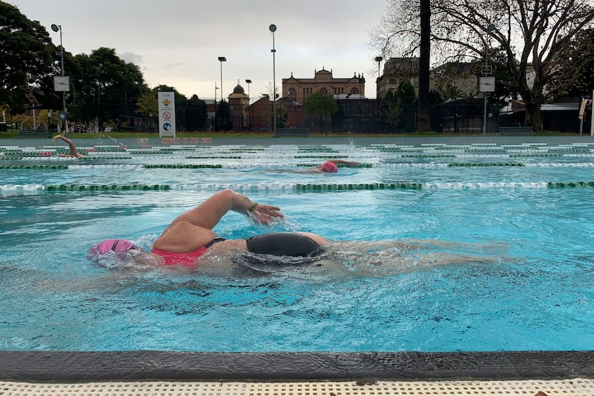 A woman swims laps in an outdoor pool on a grey day.