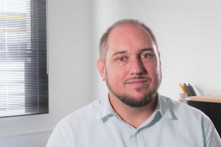 A man looks at the camera with a solemn expression