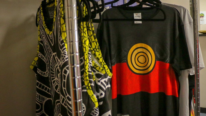 A t-shirt with the Aboriginal flag on it hangs on a rack.